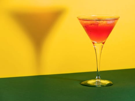 Red cocktail in a glass shaping its shadow on a green and yellow background