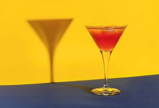 Red cocktail in a glass shaping its shadow on a blue and yellow background