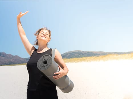 Woman in sportswear enjoying at the beach with a rolled-up mat under her arm . Copy space.