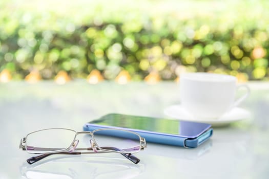 Close up Eyeglasses and smartphone on table at home with coffee cup