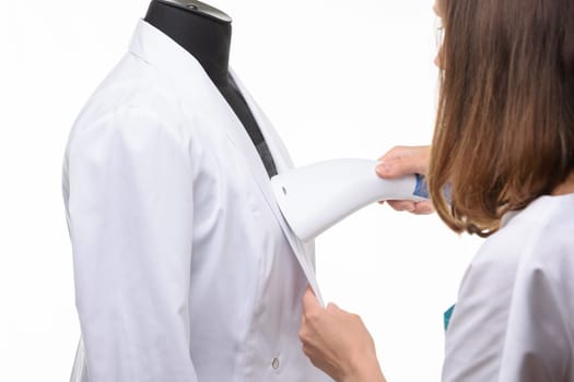 Girl handles medical clothing by steamer on a white background