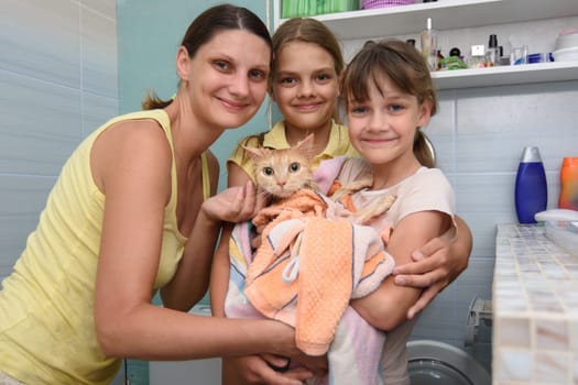 Family poses in the bathroom with wet bathed cat wrapped in towel