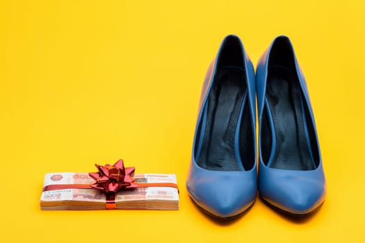 Beautiful women's shoes and a wad of money with a gift ribbon on a yellow background