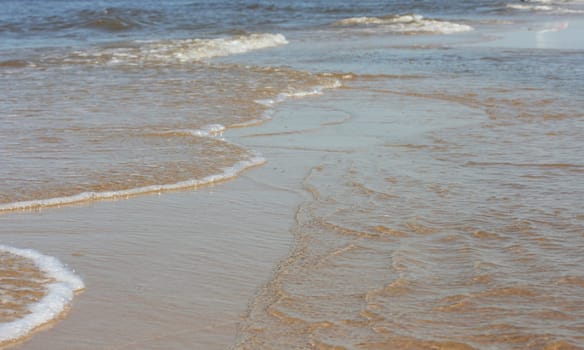 Waves with whitecaps flood the sandy beach.
