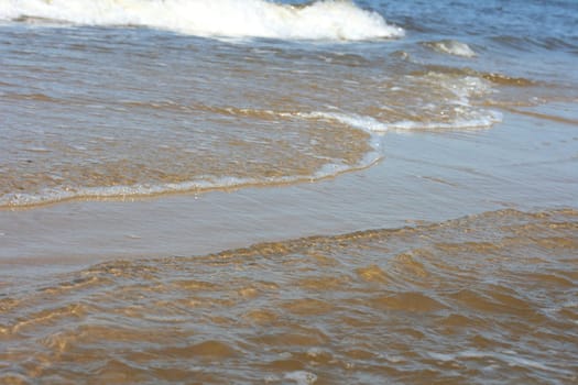 Waves with whitecaps flood the sandy beach.