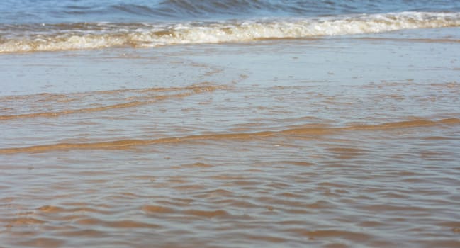 Waves with whitecaps flood the sandy beach.