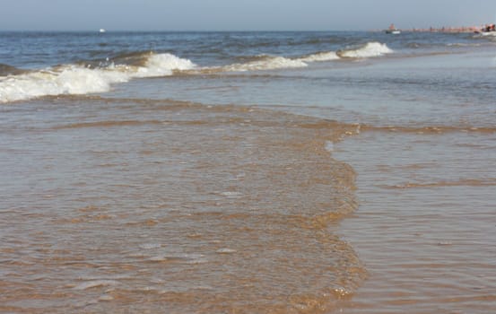 Waves with whitecaps flood the sandy beach.