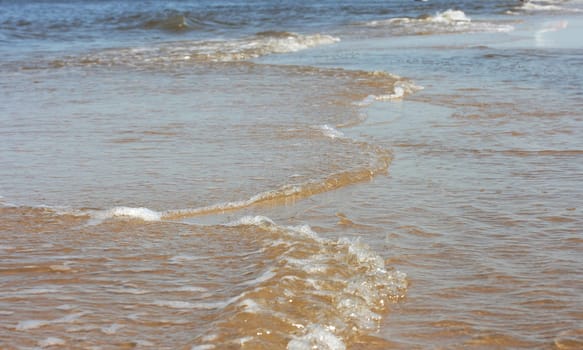 Waves with whitecaps flood the sandy beach.