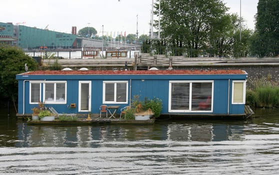 A blue house boat with white window frames and a small terrace.