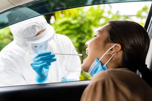 Portrait of asian woman drive thru coronavirus covid-19 test by medical staff with PPE suit by throat swab. New normal healthcare drive thru service and medical concept.