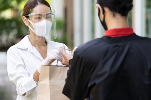 Portrait of atrractive asian woman give bakery grocery bag to delivery man to deliver it to customer make online order. Food delivery service concept in new normal after coronavirus pandemic.