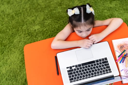 High angle view or Top View Asian girl student learning online class with video call with her teacher or tutor on computer laptop. Online education social distance and e-learning new normal concept.