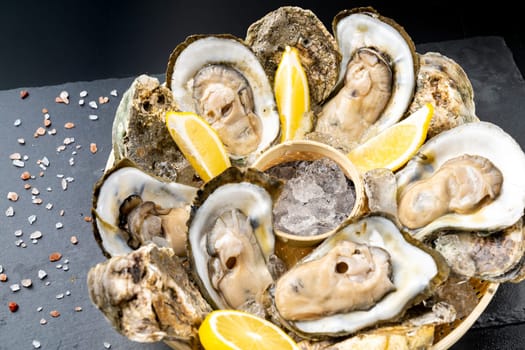 Fresh oyster serve with lemon in basket on black stone plate. Fresh seafood food and european cuisine gourmet concept.