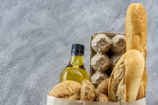 Grocery bag with egg cooking oil and variety of bread in disposable paper bag on grey vintage loft background. Bakery food and drink and grocery concept for delivery.