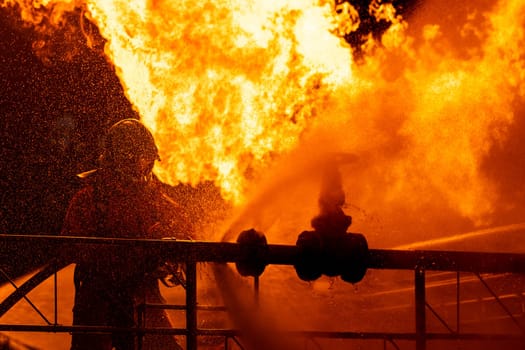 Firefighter using water fog type fire extinguisher to fighting with the fire flame from oil pipeline leak and explosion on oil rig and natural gas station. Firefighter and industrial safety concept.