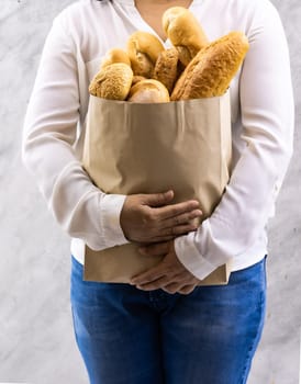 Close up of asian smile woman housewife holding variety bread in disposable paper bag on grey vintage loft background. Bakery food and drink grocery and domestic life lifestyle concept for delivery.