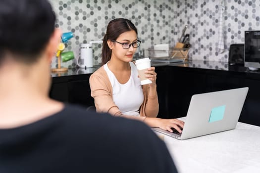 Asian woman work from home in kitchen drink take away coffee while man work in distance in foreground while city lockdown from coronavirus covid-19 pandemic. New Normal lifestyle working from home.