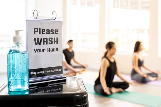 Alcohol gel or hand sanitizer with Hand wash signage to protect from COVID-19 coronavirus pandemic in new normal fitness gym with background of yoga class students and trainer.