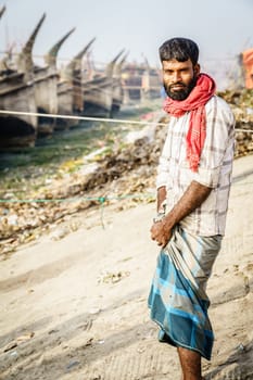 Chittagong, Bangladesh, December 23, 2017: Portrait of a middle-aged fisherman with traditional fishing boats in the background
