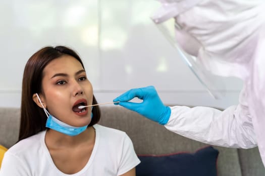 Medical staff with PPE suit test coronavirus covid-19 to asian woman by throat swab at home. New normal healthcare service at home and medical delivery concept.
