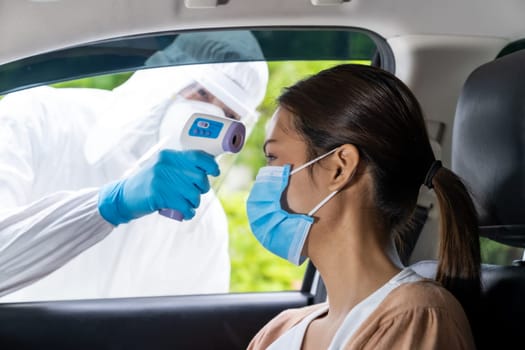 Medical staff with PPE Take Temperature for fever to asian woman before coronavirus covid-19 test at drive thru station in hospital. New normal healthcare drive thru service and medical concept.