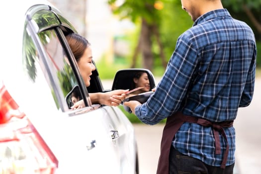 Back view of asian woman customer make mobile payment contactless technology on drive thru food service restaurant while picking up. Drive through is more popular after coronavirus covid-19 pandemic.