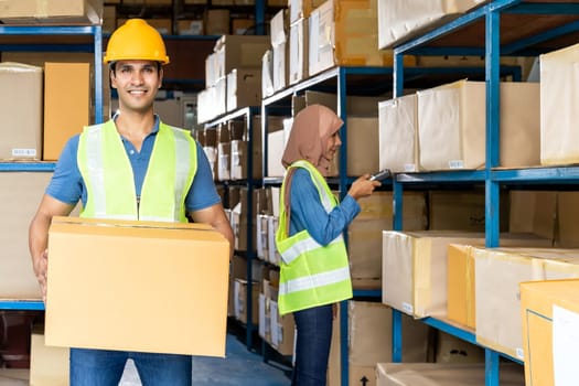 Portrait of Indian warehouse worker hold cardboard box packaging with muslim asian worker do inventory in warehouse distribution center environment. Using in business warehouse and logistic concept.