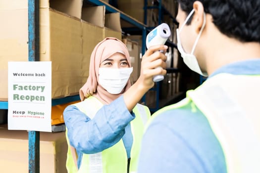 Islam asian warehouse worker take temperature to worker before getting in factory after reopening after city lockdown from COVID-19 coronavirus pandemic in warehouse distribution center environment.