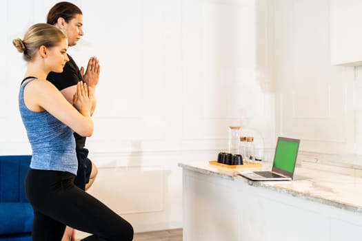 White caucasian fit sporty couple doing yoga tree pose in living room at home watching online tutorials from trainer on laptop. Working out, fitness sport and healthy lifestyle concept.