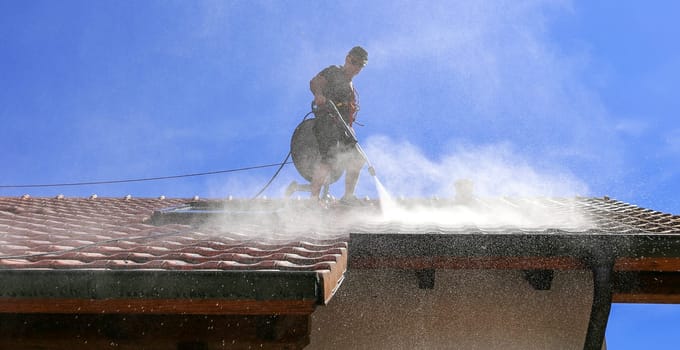 Workers cleaning the roof of moss and dirt with a high pressure cleaner. Secured with a safety rope.