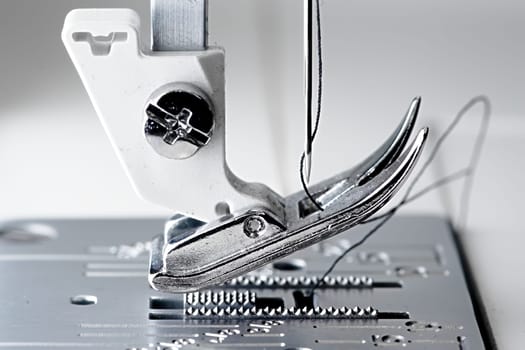 4 - Super macro image with selective focus on the needle and thread. Shows mechanism and working area of a white and metal sewing machine.