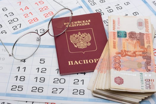 Glasses, passport and a bundle of money are on the sheets of a wall calendar