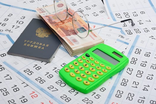 Labor book, a bundle of money, glasses and a calculator lies on the background from the calendar