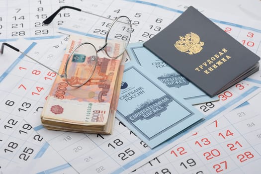 Anapa, Russia - 29.06.2020: On the background of the calendars lie a work book, a savings book, a bundle of money and glasses