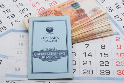 Anapa, Russia - 29.06.2020: On a bundle of five-thousandth Russian banknotes lies a savings book, a background of calendar sheets