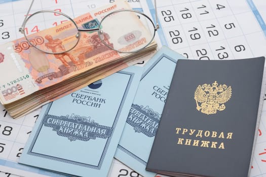 Anapa, Russia - 29.06.2020: Savings and work book, a pack of Russian rubles and glasses lie on the calendar