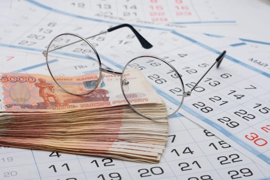 A stack of five thousandth bills and glasses are on the calendar