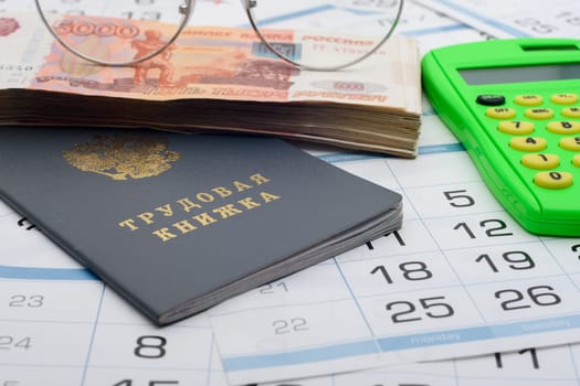 Labor book of the Russian Federation, on it is a bundle of five-thousandth bills, glasses and a calculator