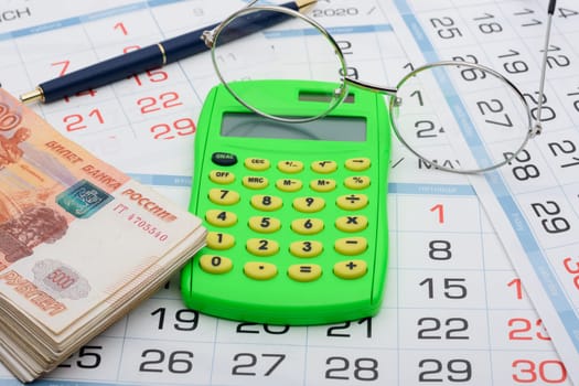 Calculator in the center of the frame, money on the sides, a pen and glasses