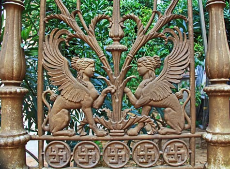 Decorative metal fence with two mythical sphinxes facing each other and a swastika border in Athens, Greece.