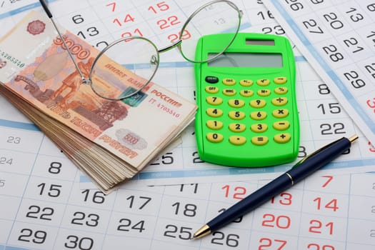 Money, glasses, calculator and pen lie on the calendar