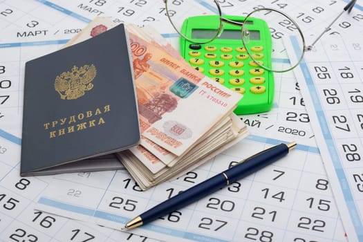 A bundle of five-thousandth bills sticks out of the work book, next to it lies a calculator and glasses and a pen