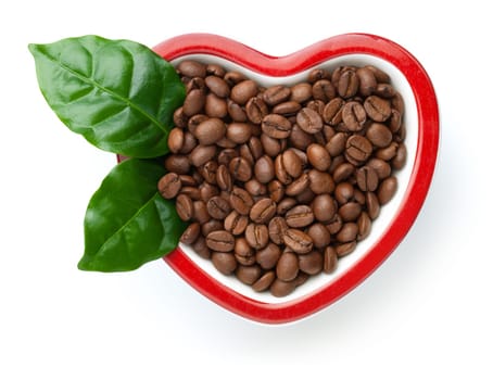 Coffee beans in heart shaped bowl isolated on white background. Roasted arabica with fresh green leaves. View from above