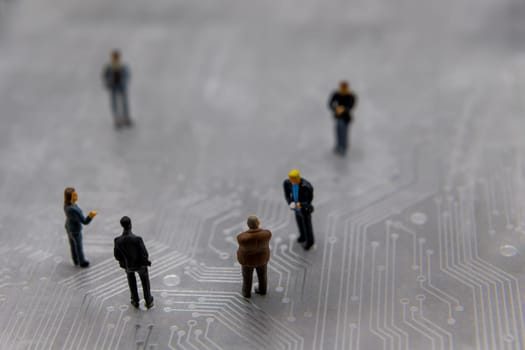 Miniature figurines posed as business people in a meeting over abstract futuristic circuit board, future business concept
