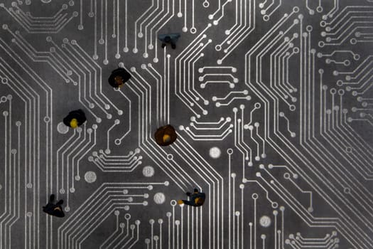 Miniature figurines posed as business people in a meeting over abstract futuristic circuit board, future business concept