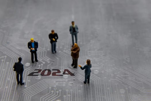 Miniature figurines posed as business people in a meeting over abstract futuristic circuit board with text year 2024