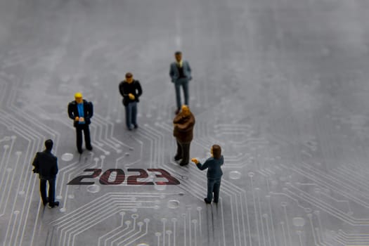 Miniature figurines posed as business people in a meeting over abstract futuristic circuit board with text year 2023