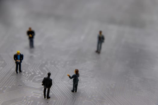 Miniature figurines posed as business people in a meeting over abstract futuristic circuit board, future business concept