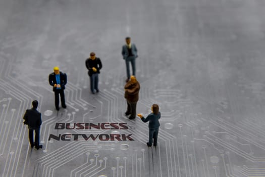 Miniature figurines posed as business people in a meeting over abstract futuristic circuit board with text Business Network