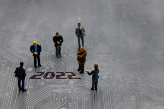 Miniature figurines posed as business people in a meeting over abstract futuristic circuit board with text year 2022